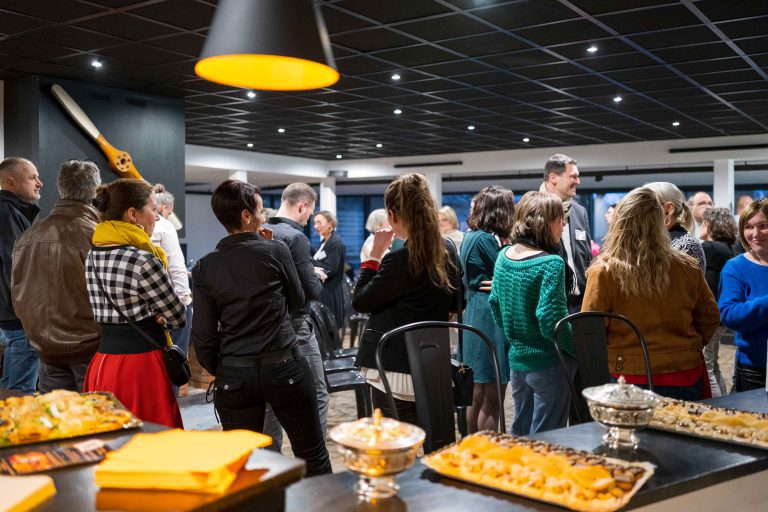 Conférence · Réseau Les Leaders du Business. Reportage évènementiel. Personnes discutant lors d'un évènement réseau, avec au premier plan flou des plateaux avec des mets salés et sucrés.