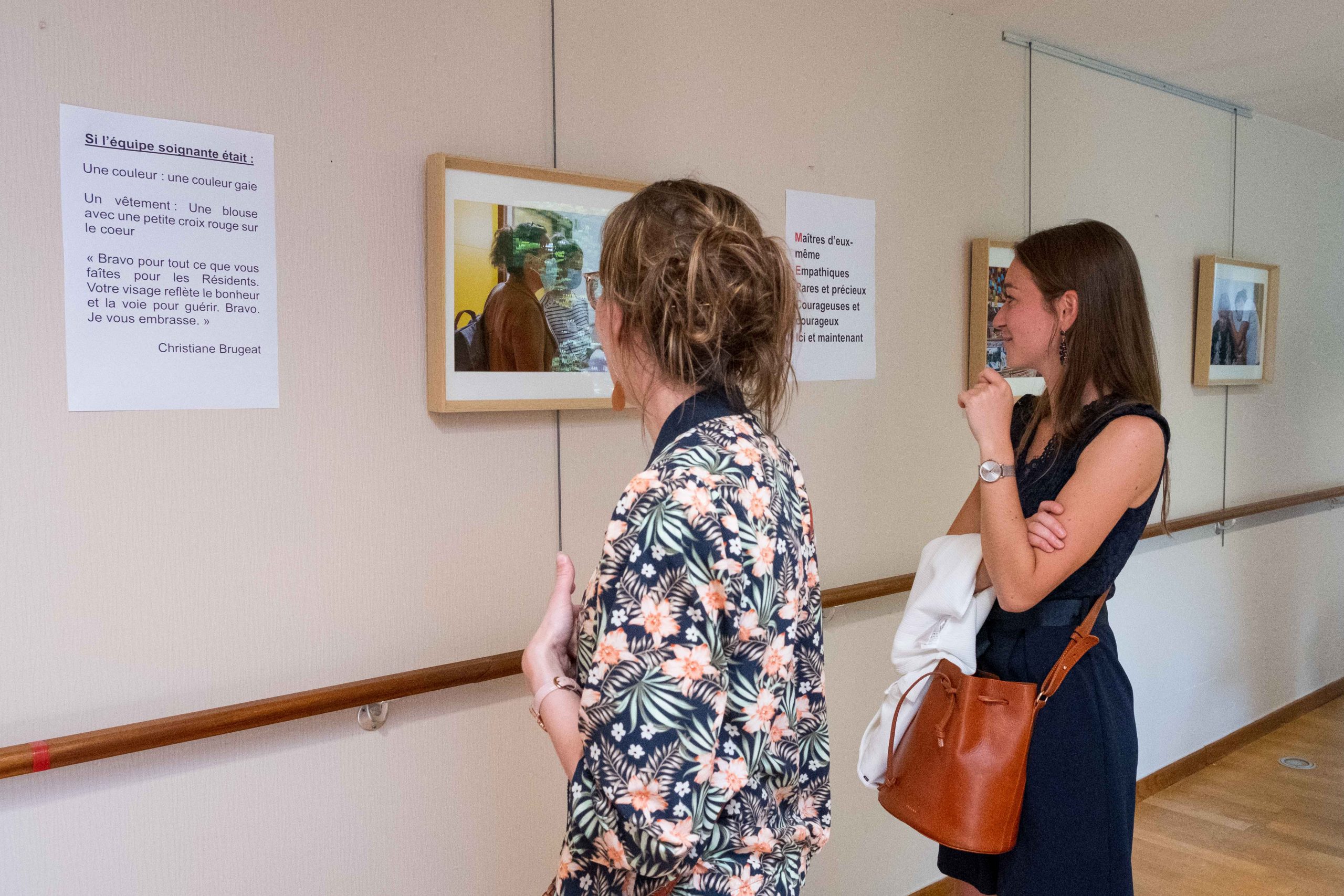 Deux personnes regardant les photos et les textes accrochés au mur, à l'occasion du vernissage d'une exposition au sein d'un EHPAD