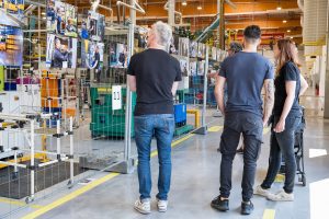 Reportage évènementiel. Lors des portes ouvertes de l'usine, un groupe de personnes regarde avec attention les photographies exposées à la fin du parcours (issues du reportage métier réalisé au sein de l'entreprise)